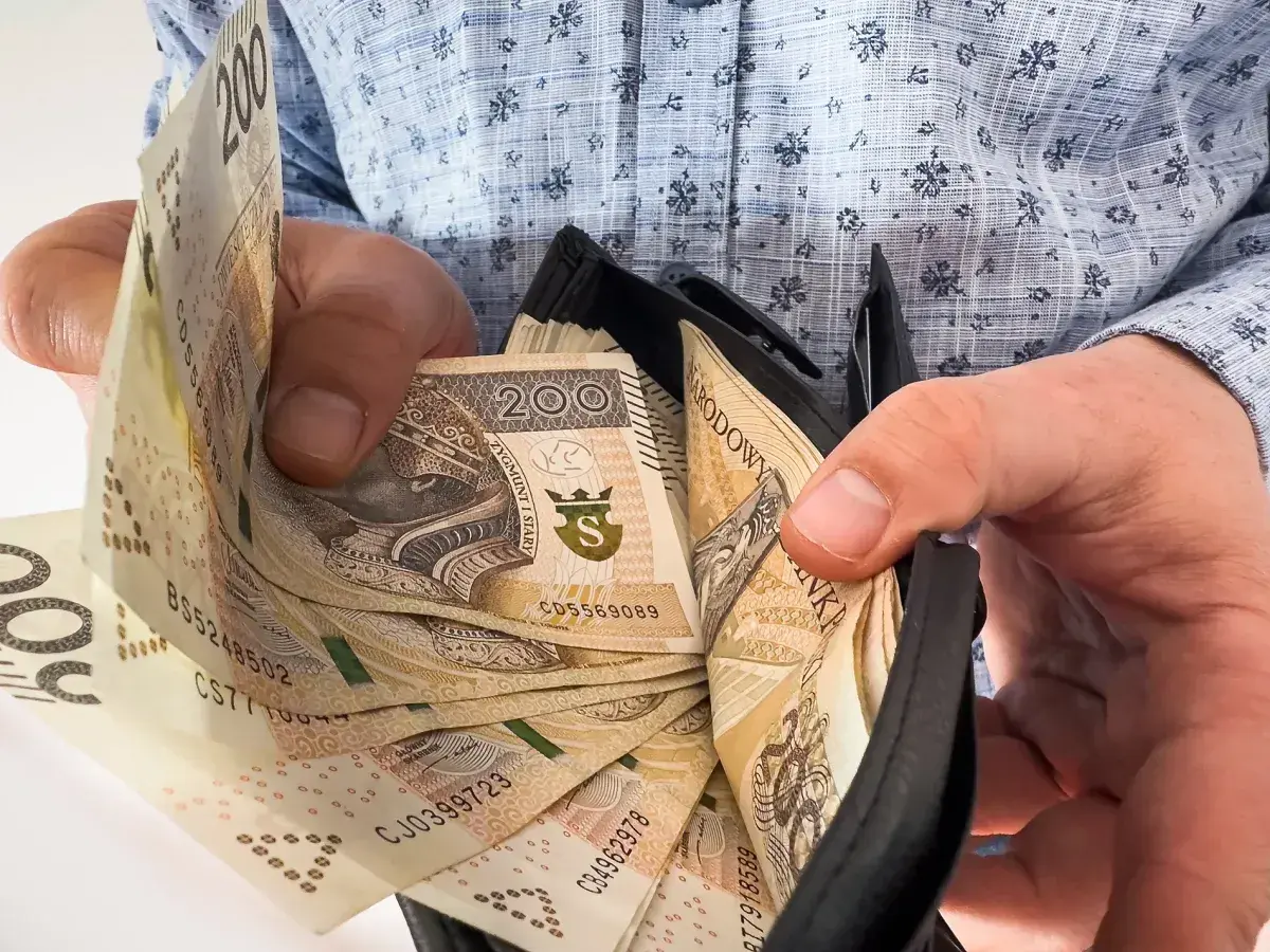 Dłonie trzymające portfel z polskimi banknotami 200 zł.