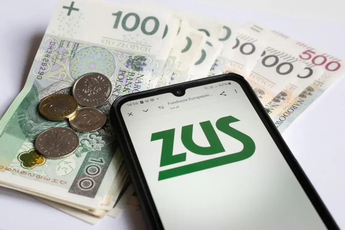 Polskie banknoty i monety obok smartfona z logo ZUS.