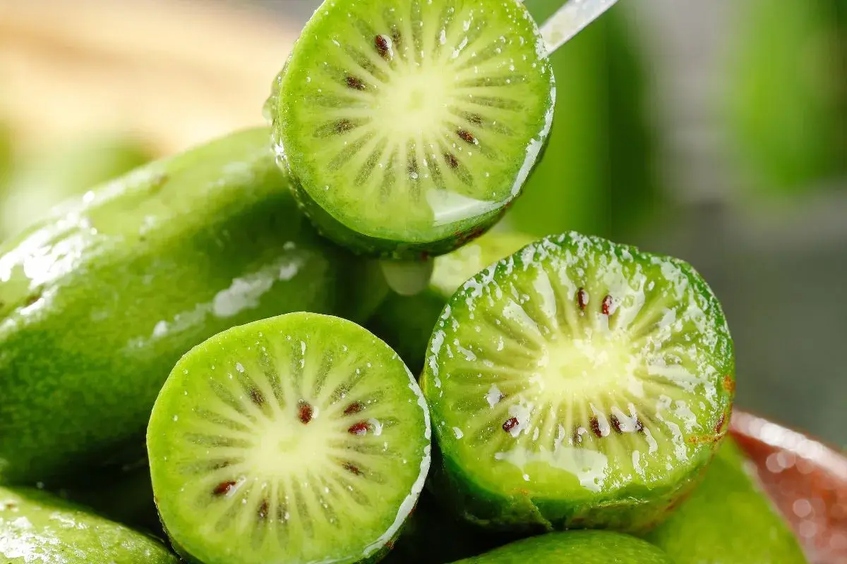 Przekrojone na pół, mokre kiwi z widocznymi pestkami na tle innych owoców.