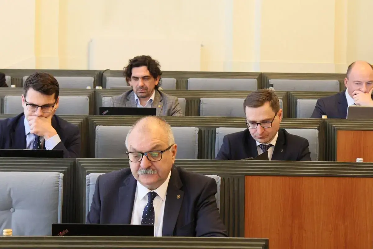 Mężczyźni w garniturach siedzą w rzędach, patrząc na laptopy.