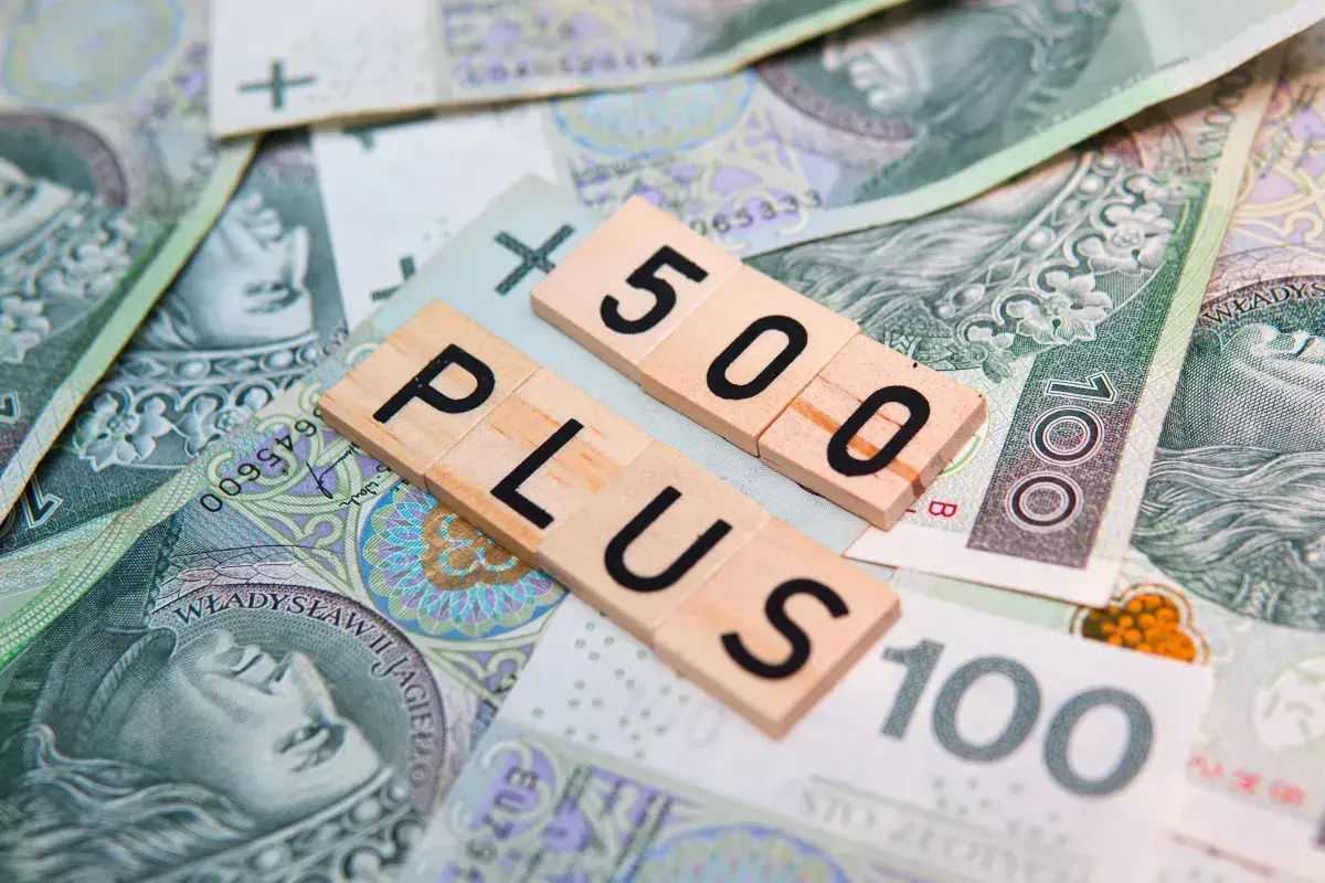 Litery "500 PLUS" na tle polskich banknotów. Symbol wsparcia finansowego, np. 500 plus dla niepełnosprawnych.