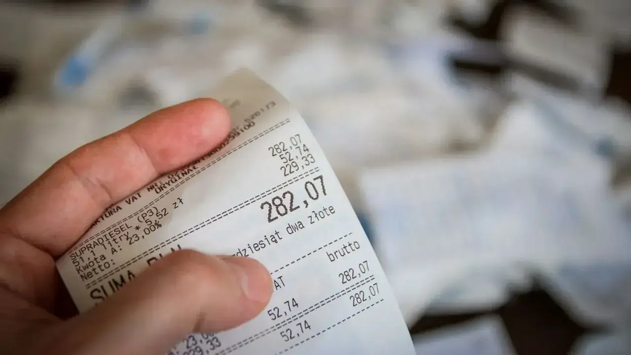 Dłoń trzyma paragon z widoczną kwotą 282,07 zł.