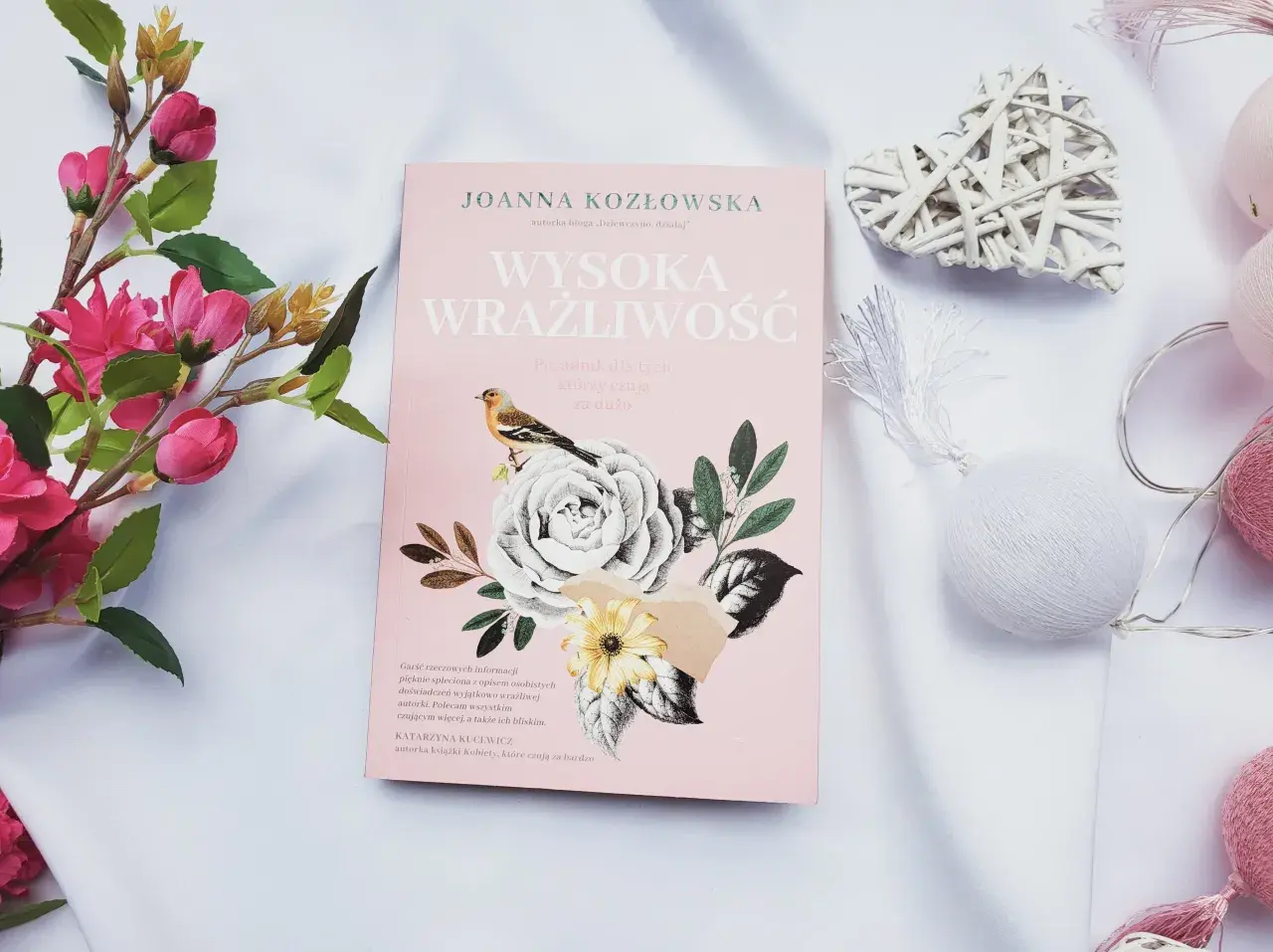 Różowa okładka książki "Wysoka wrażliwość" z motywem kwiatów i ptaszka, otoczona dekoracjami.