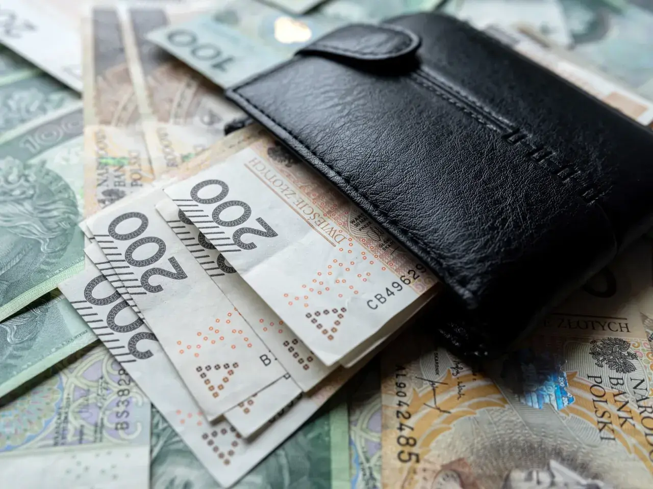 Czarny portfel na stosie polskich banknotów 100 i 200 zł.