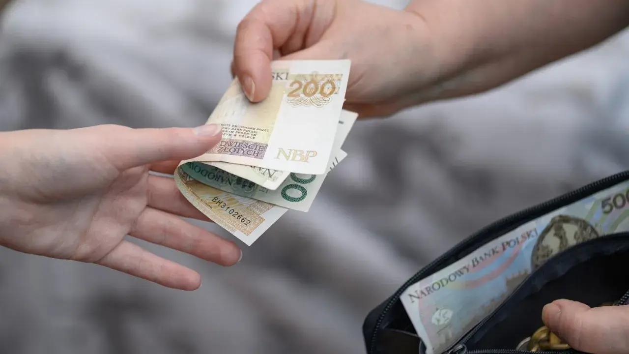 Dwie ręce przekazują sobie polskie banknoty 200 zł i 500 zł z portfela.