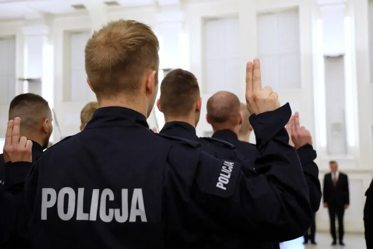 Policjanci w mundurach z napisem "POLICJA" podnoszą ręce z dwoma palcami uniesionymi do góry.
