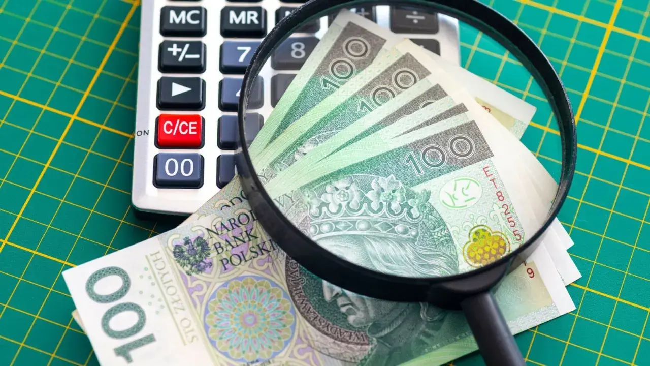 Kalkulator, szkło powiększające i banknoty 100 zł na zielonej macie.