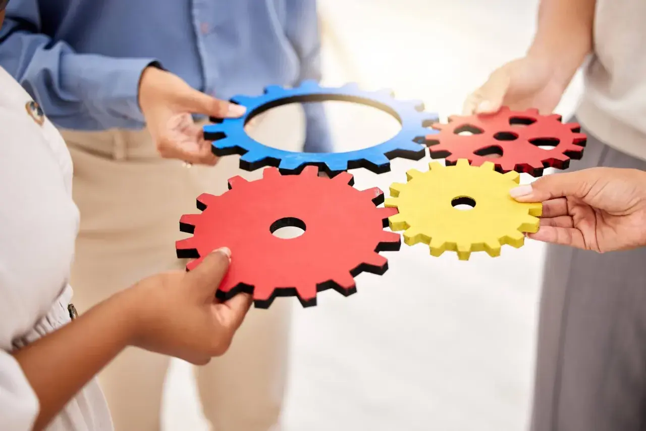 Dłonie łączą kolorowe trybiki, symbolizując współpracę i mechanizm.