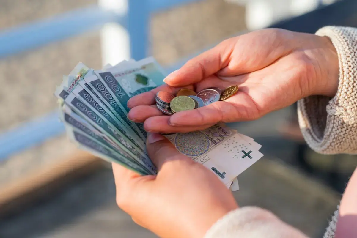 Dłonie trzymające polskie banknoty i monety.