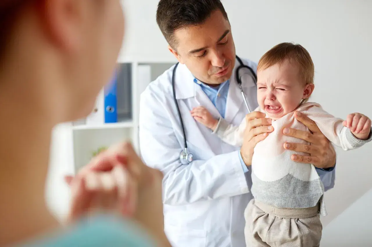 Lekarz uspokaja płaczące dziecko, które przechodzi trudny skok rozwojowy. Mama patrzy z troską.