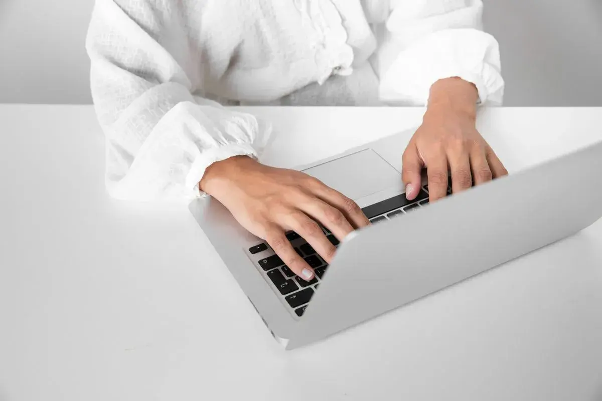 Dłonie piszące na klawiaturze laptopa na białym biurku.