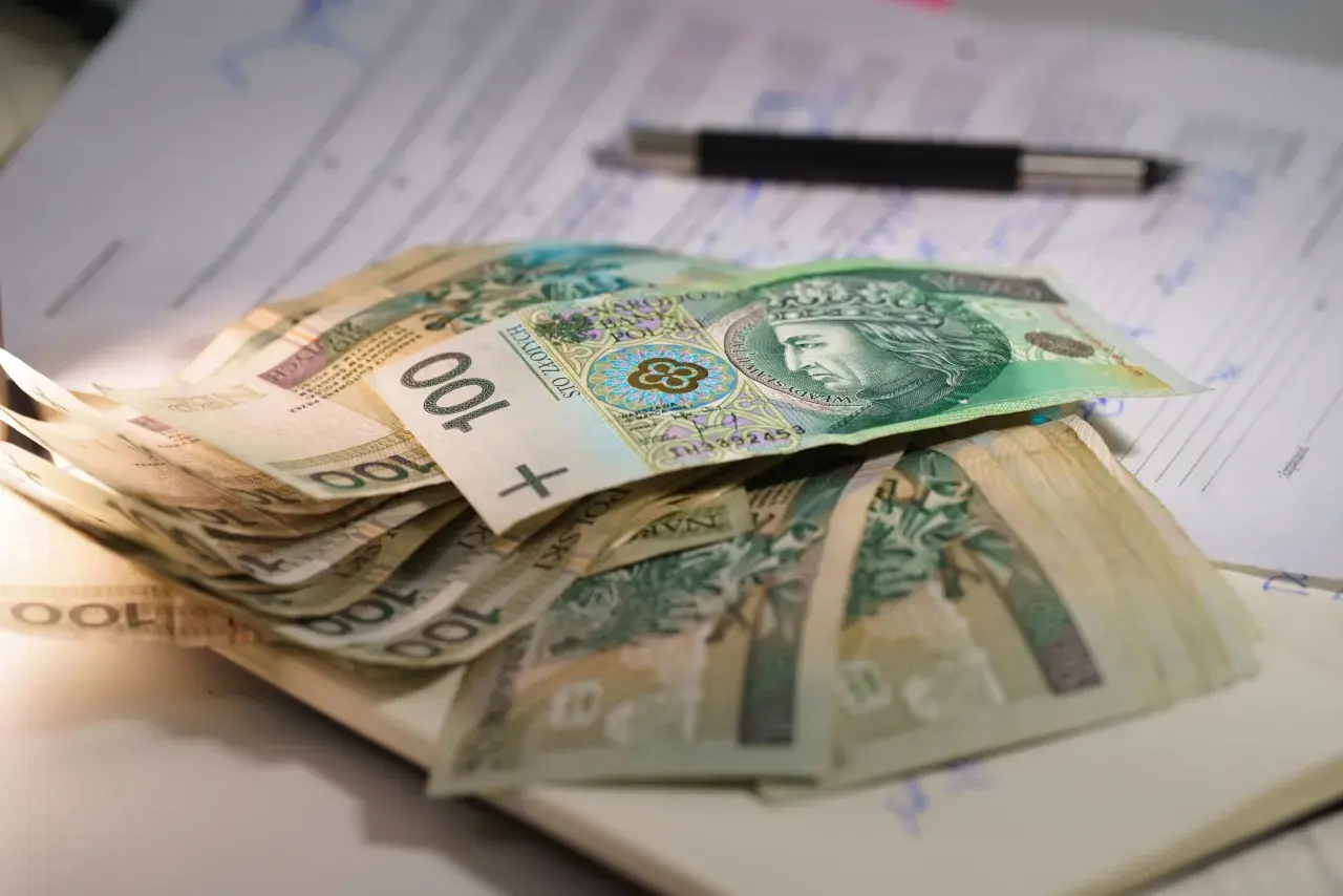 Stos banknotów 100 zł leży na dokumentach. Może to być związane z oceną stopnie niepełnosprawności i przyznawanymi świadczeniami.