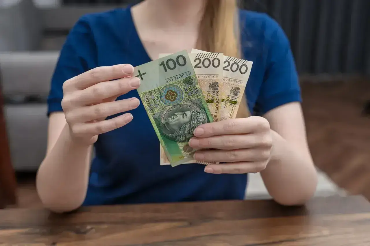 Dłonie trzymające polskie banknoty: 100 zł i dwa razy po 200 zł.