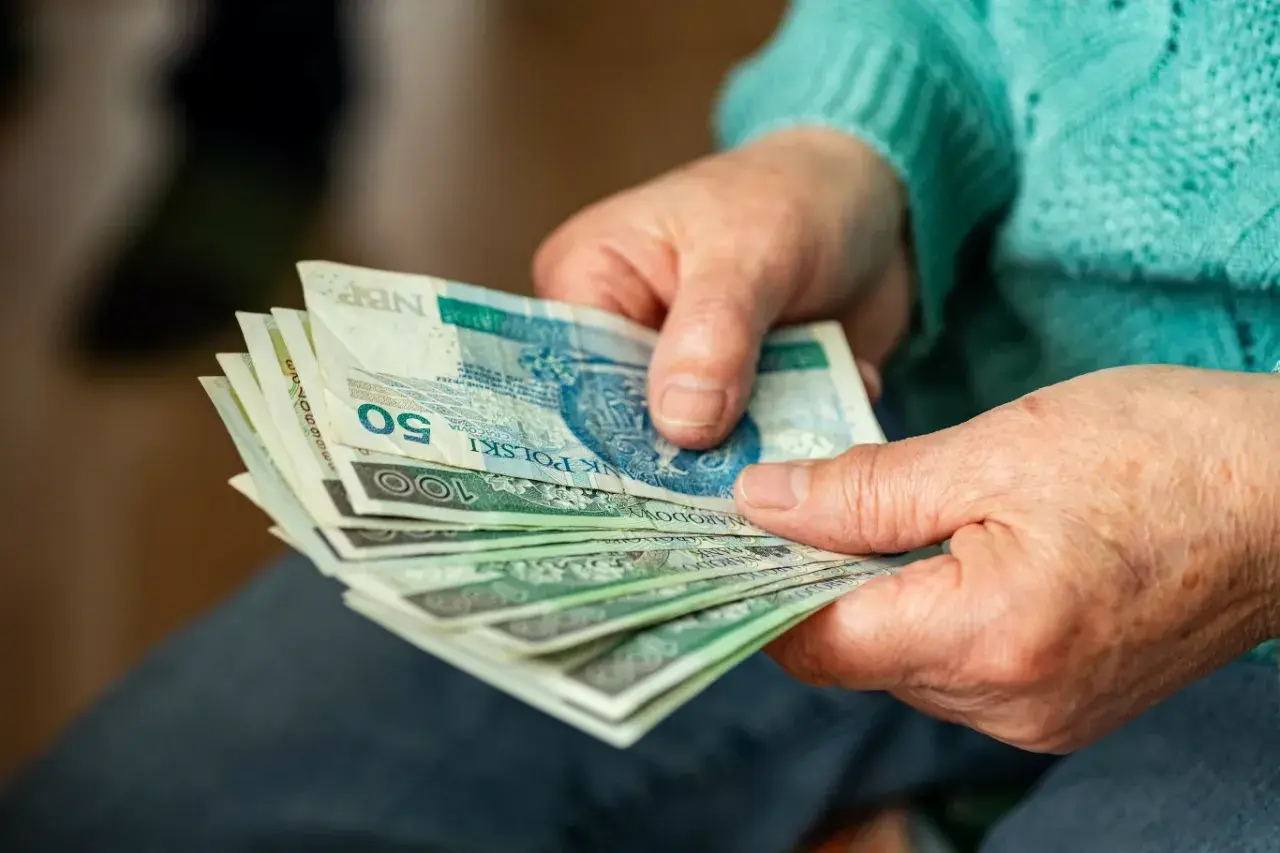 Dłonie starszej osoby trzymające stos polskich banknotów.