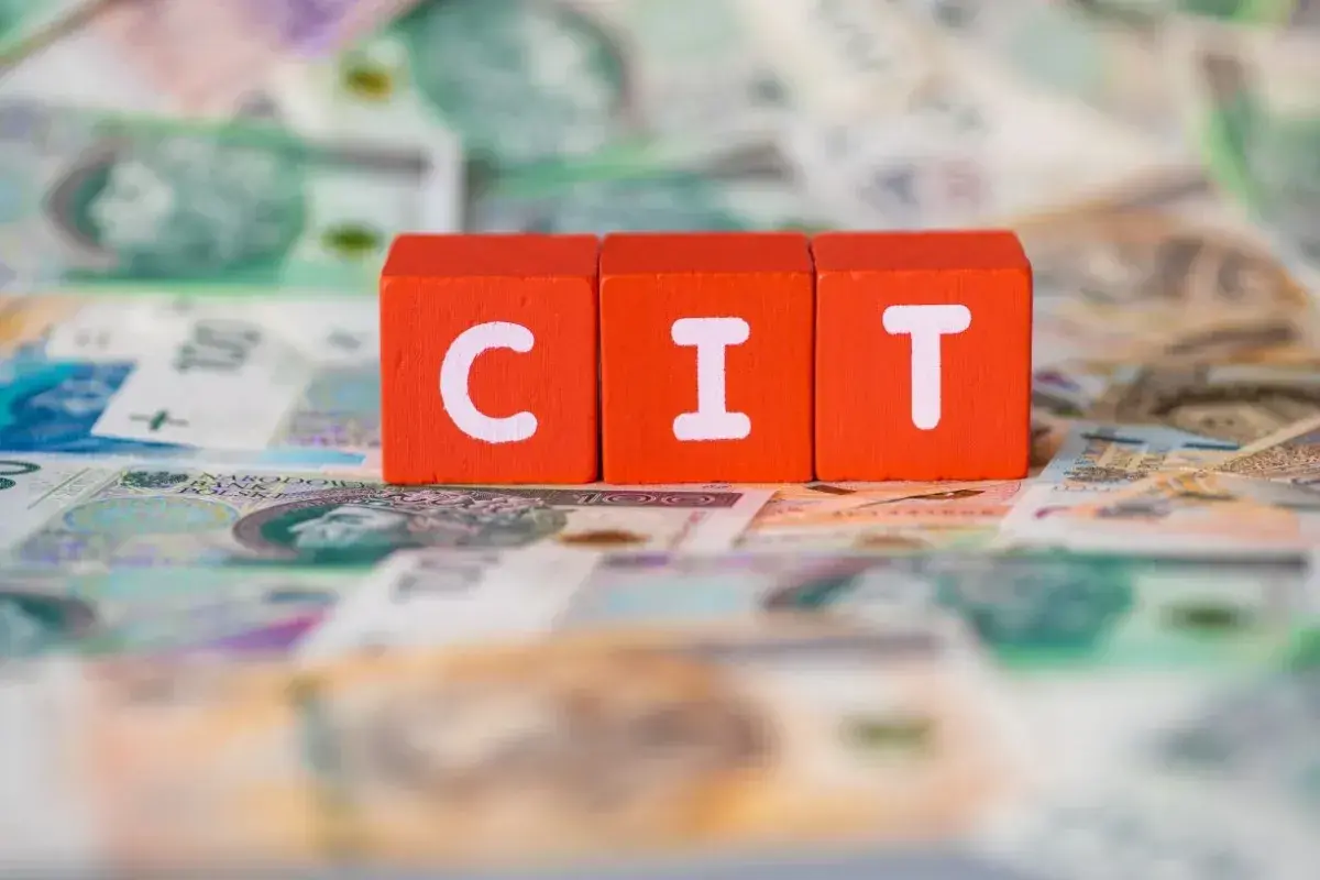 Czerwone klocki z literami "C", "I", "T" leżą na banknotach. Podatek CIT to ważna kwestia dla firm.