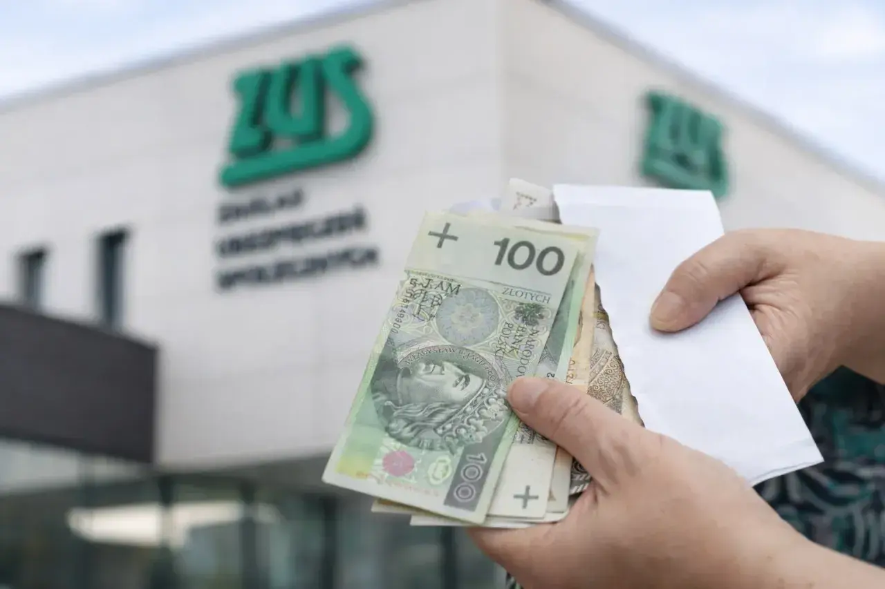 Dłonie trzymające polskie banknoty 100 zł przed budynkiem ZUS.