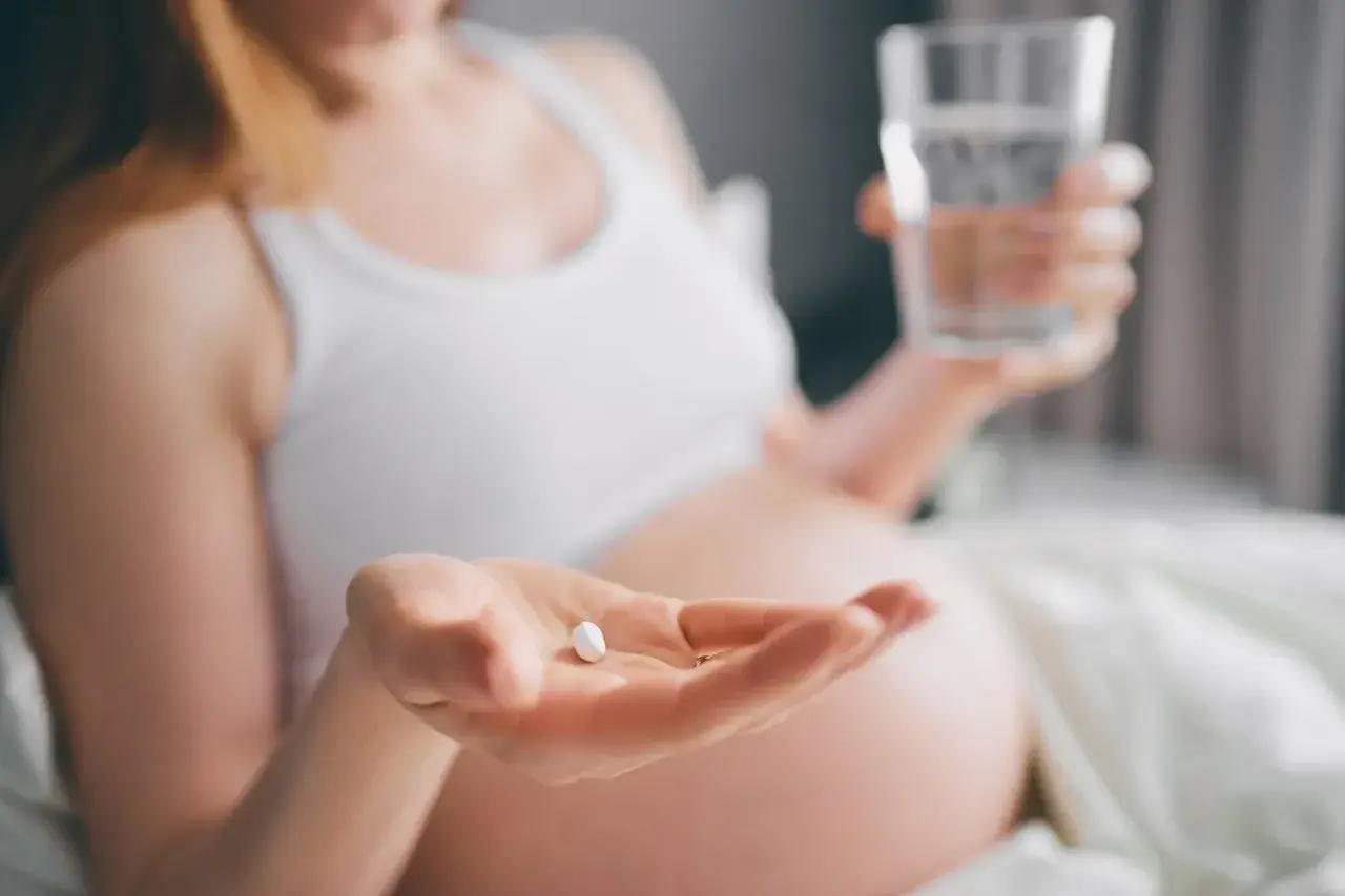 Kobieta w ciąży bierze tabletkę i popija ją wodą, dbając o prawidłowe ciśnienie w ciąży.