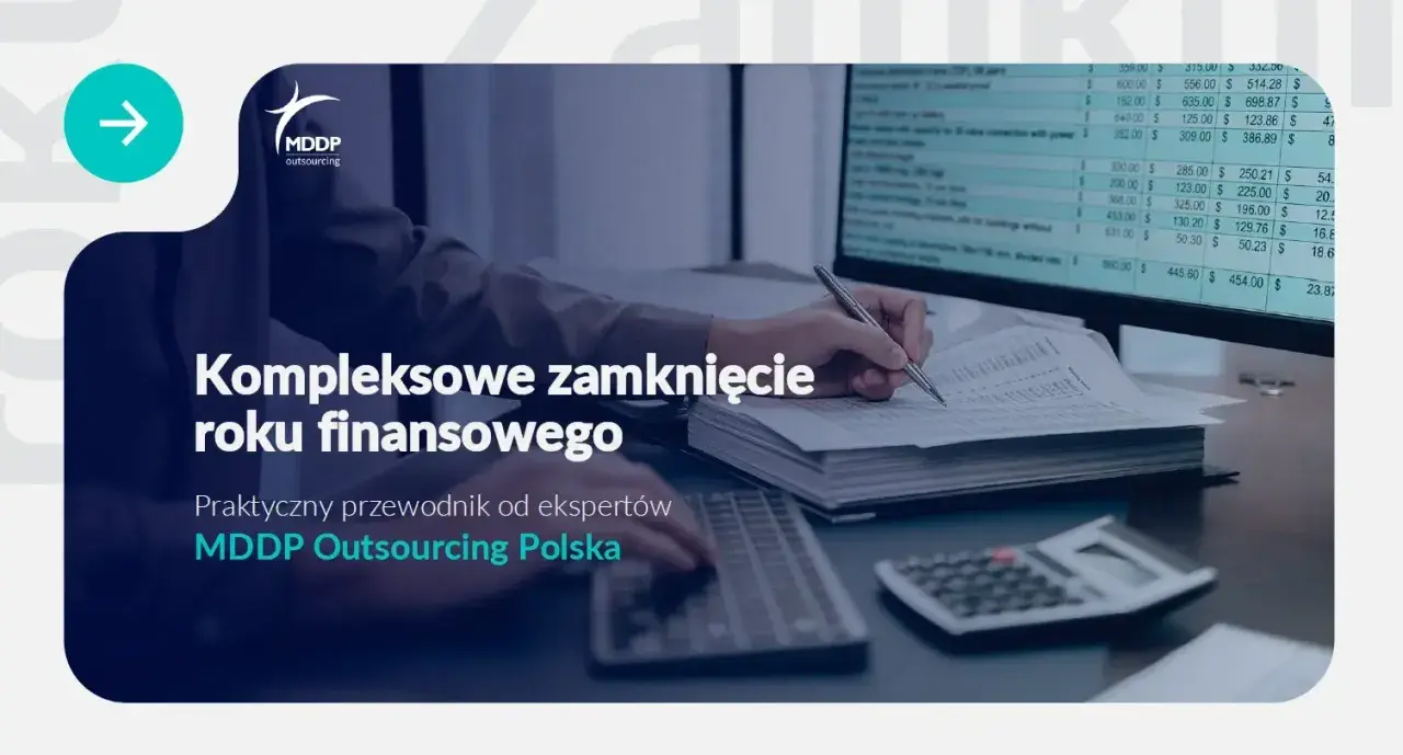 Osoba pisząca ręcznie na dokumentach przy biurku z komputerem i kalkulatorem.