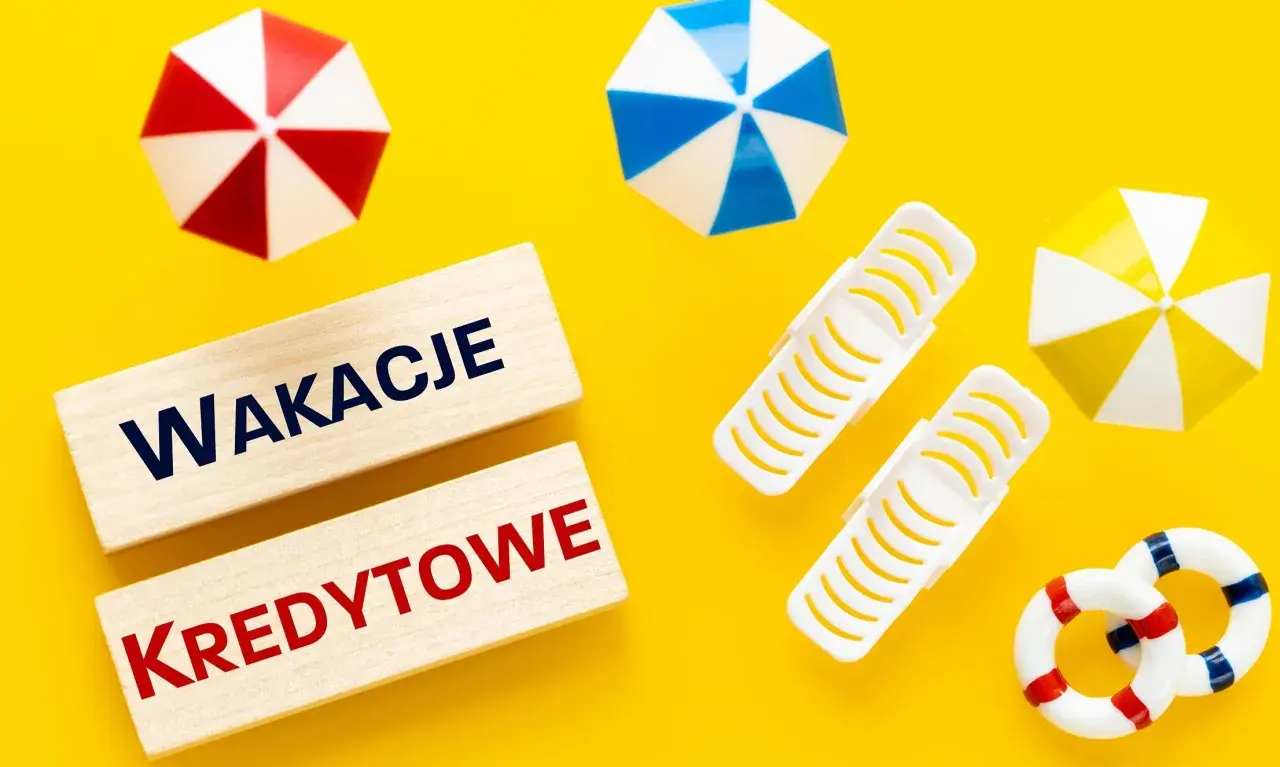 Drewniane klocki z napisem "Wakacje Kredytowe" na żółtym tle, otoczone miniaturowymi parasolkami plażowymi i kołami ratunkowymi.
