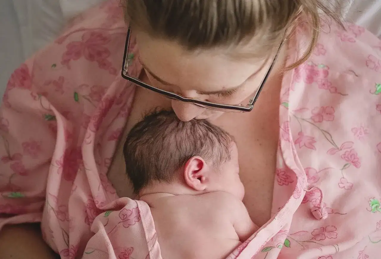 Mama całuje główkę swojego noworodka. To piękny moment kangurowania, pełen miłości i bliskości.