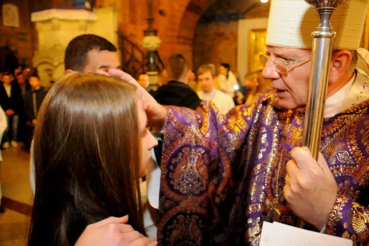 Biskup namaszcza głowę młodej dziewczyny. To ważny moment, który jest częścią mojej motywacji, dlaczego chcę przyjąć sakrament bierzmowania.