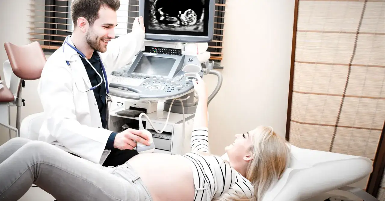Uśmiechnięty lekarz wykonuje badanie USG ciężarnej kobiety, która z radością obserwuje obraz na monitorze. To piękny moment ciąży.